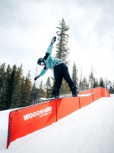 Persona realizando una maniobra de snowboard sobre un riel rojo en un parque de nieve.